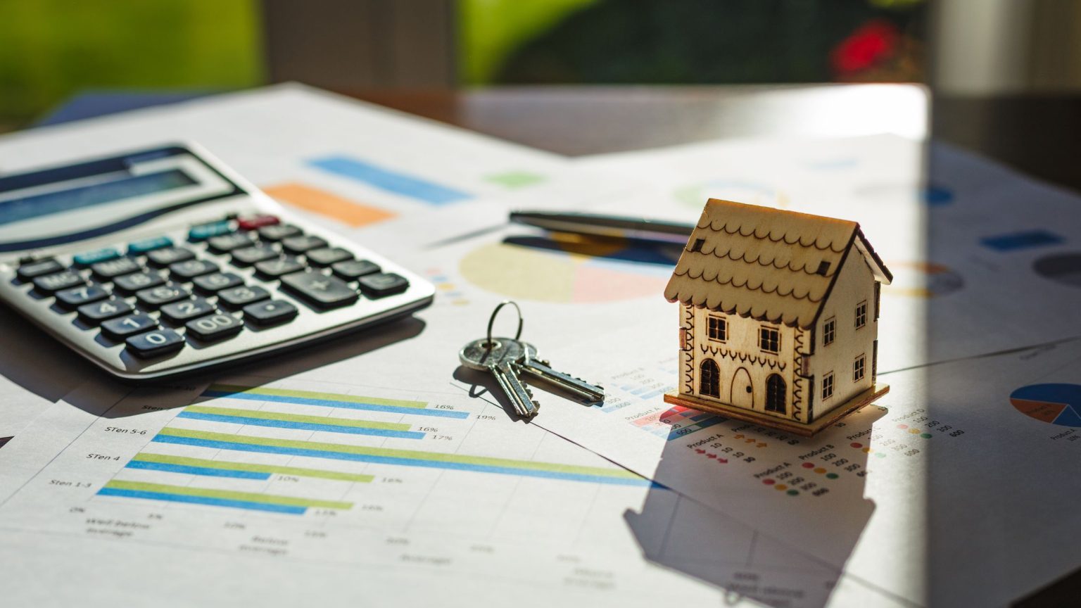 Model house, keys, and a calculator resting on printed housing market charts
