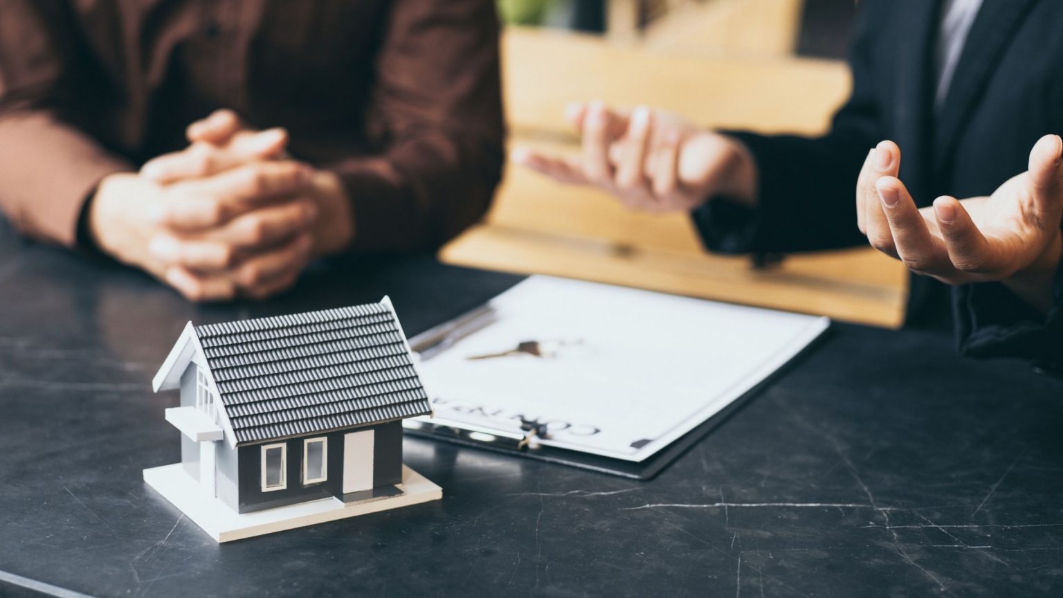 Two people discussing mortgage options at a desk with a small model house and loan documents