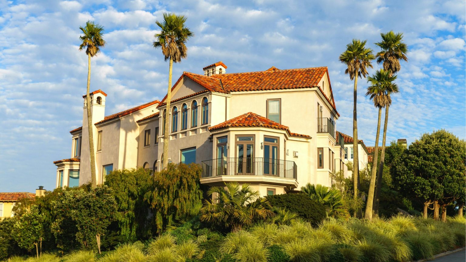 Large Mediterranean-style luxury home with a red tile roof framed by tall palm trees