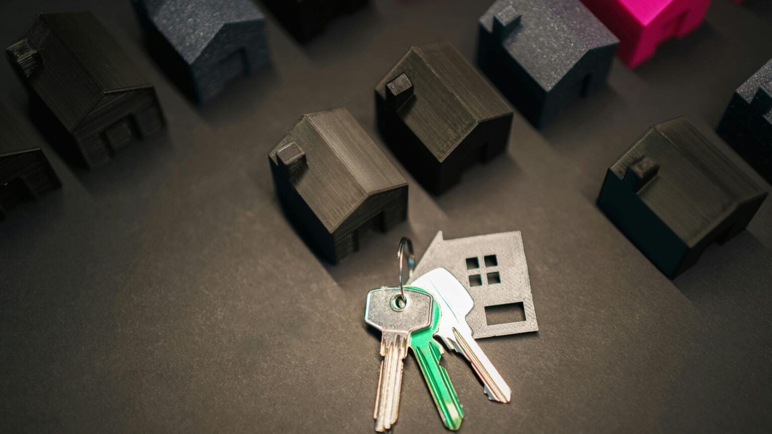 Rows of small dark model houses with a set of house keys on a table, illustrating housing market trends