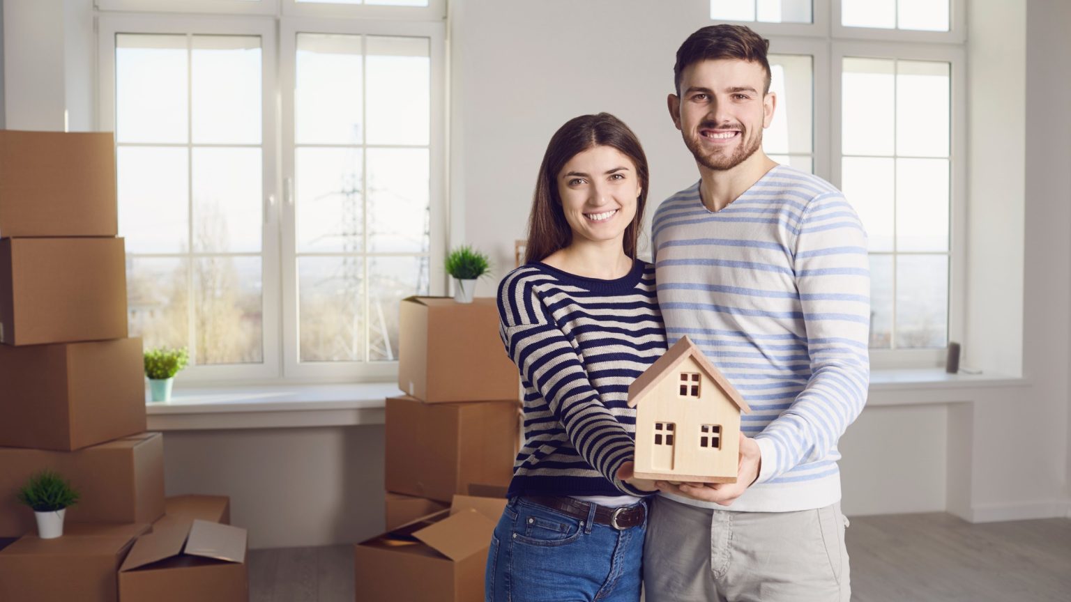 Smiling young couple holding a small model house in a new home surrounded by moving boxes
