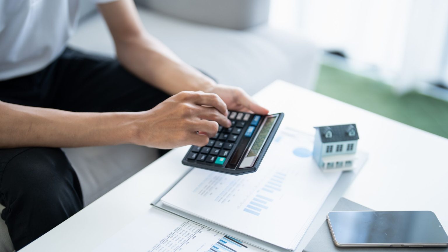 Person using a calculator beside a small model house while planning a home savings budget