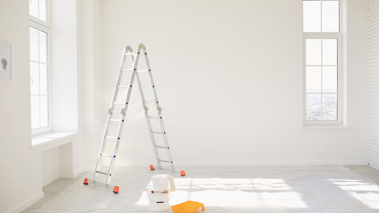 Empty white room with a stepladder and paint supplies, ready for repairs before a home sale