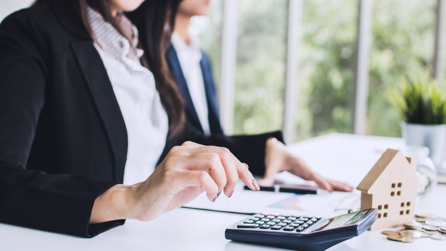 Homeowner reviewing refinance paperwork with a calculator and small model house on the desk